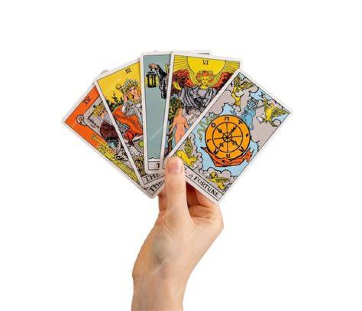 Roya holding tarot cards, surrounded by lit candles, small mirrors, and framed photos