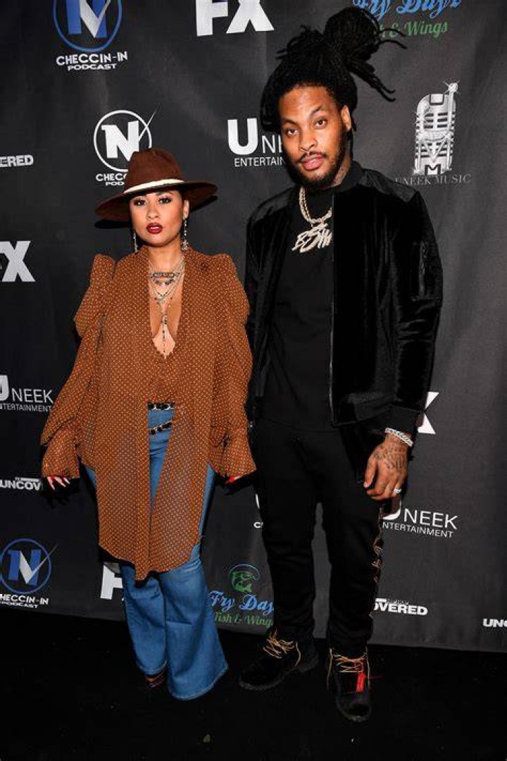 Tammy Rivera in brown and Waka Flocka Flame in black posing on read carpet together.
